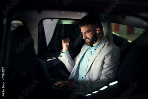 Elegant modern businessman with laptop on the back seat celebrating job success.