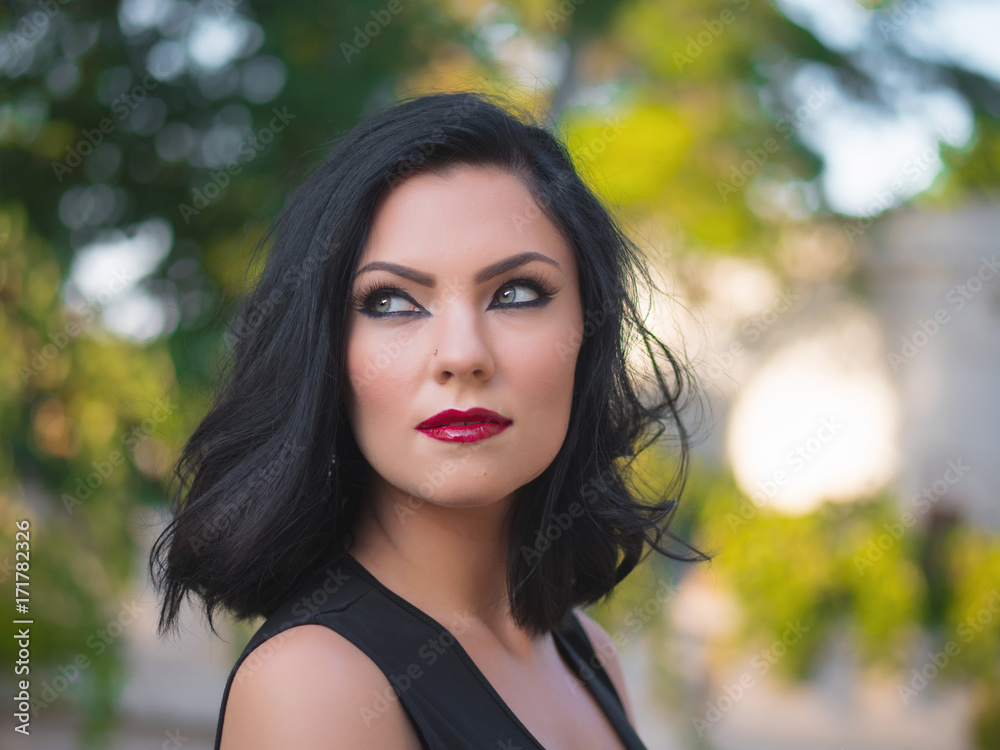 Portrait of young sexy brunette woman with evening arabic make-up and hairstyle posing on street at summer. Oriental make up with long arrows and red shining lips. Trend 2018. Portrait of young sexy brunette woman with evening arabic make-up and hairstyle posing on street at summer. Oriental make up with long arrows and red shining lips. Trend 2018.