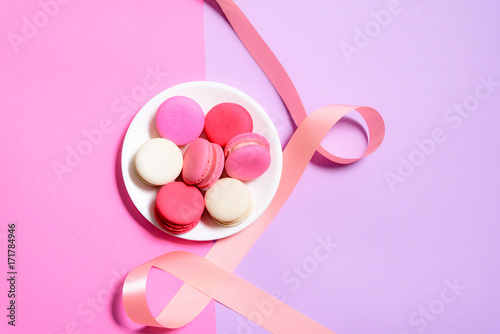 Homemade Colorful macaroons or macaron on White plate with copyspace on pink and purple background