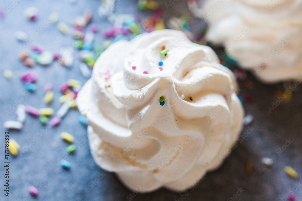Beautiful italian meringue cookies on dark gray background with colorful sprinkles. Selective focus, close up