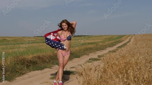 American Flag.  Sexy girl in a bikini with a flag in her hands is running along a country road