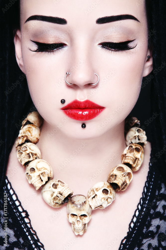 Close-up portrait of young beautiful gothic pierced woman with necklace of human sculls