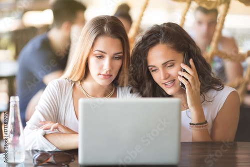 Two beautiful young women looking at laptop and laughing at bar