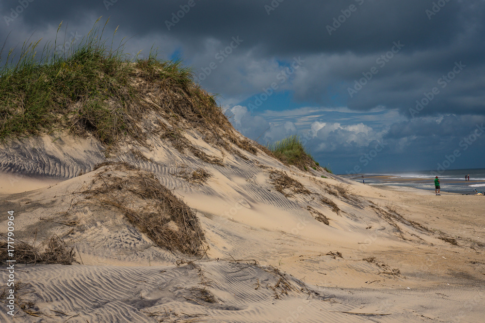 Scenic view of large sand dune in Outer Banks with big white clouds and view of ocean Scenic view of large sand dune in Outer Banks with big white clouds and view of ocean