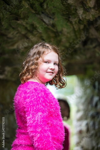 Young little girl portrait looking and smiling at the camera while exploring in an old castle © Chris