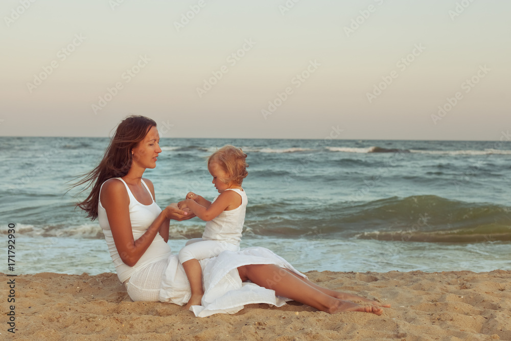 Mom and daughter are sitting on the sand on the beach near the sea