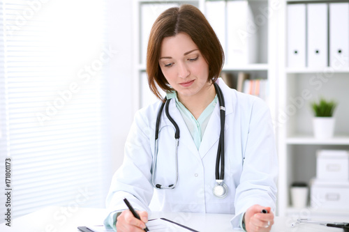 Young brunette female doctor sitting at the table and working at hospital office. 