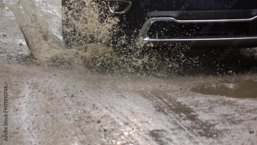 SLOW MOTION CLOSE UP Detail of a SUV car tyre driving over deep puddle and splashing water