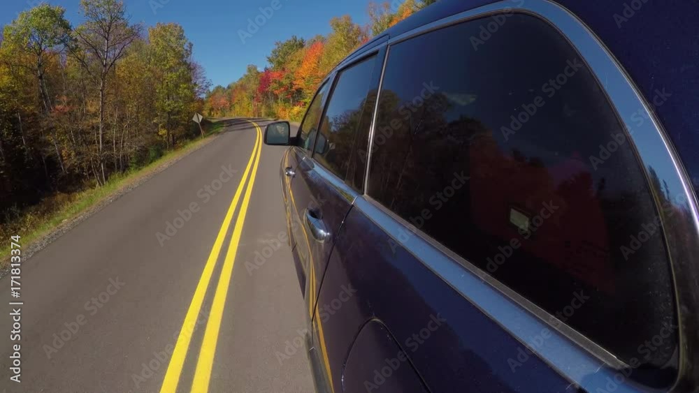 CLOSE UP LENS FLARE: Black SUV car driving along gorgeous forest road past the colorful trees on sunny autumn day. People on leaf peeping road trip traveling through bright autumn forest in sunny fall CLOSE UP LENS FLARE: Black SUV car driving along gorgeous forest road past the colorful trees on sunny autumn day. People on leaf peeping road trip traveling through bright autumn forest in sunny fall