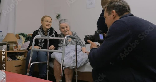 Family coming to see grandmother in the hospital. Man taking photo of elderly woman with adult granddaughter photo