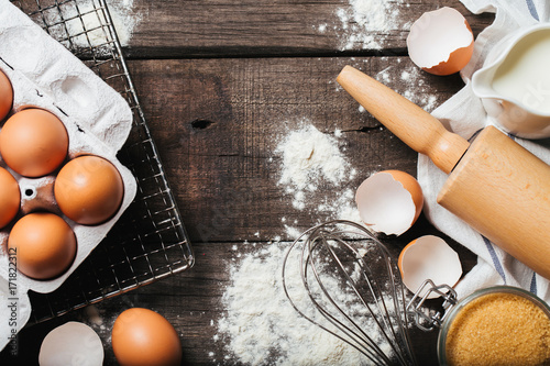 Baking or cooking wooden background with flour, sugar, eggshell and rolling pin. Top view