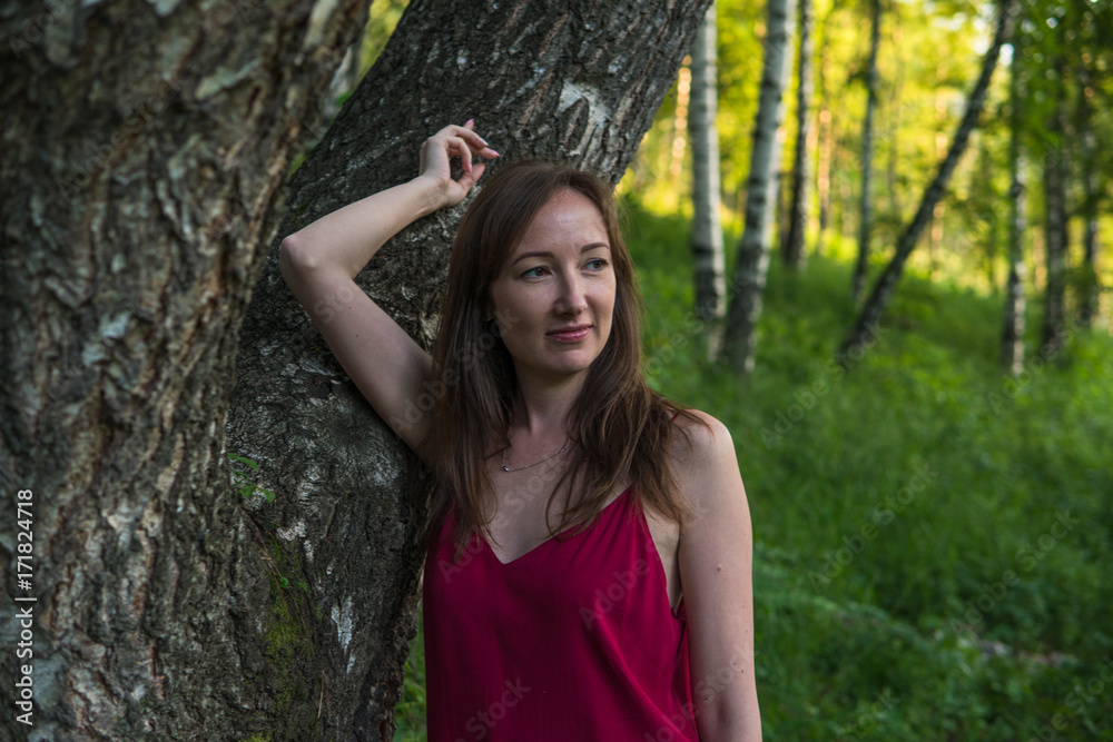 Young woman portrait in a summer forest in the mountains. Pretty girl in red dress in summertime