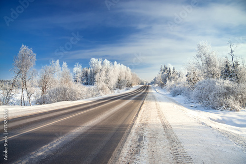 winter landscape with asphalt road,forest and blue sky.
