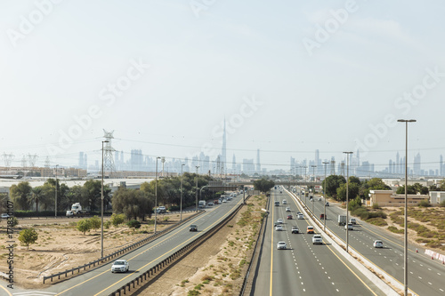 Main road with desert and electricity posts and silhouette buildings in background at Dubai. 