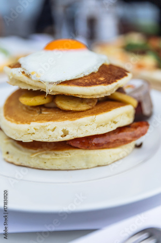 Pancakes with deep fried bacon, fried potato with peel and fried egg on the top served with maple syrup at restaurant in Dubai.