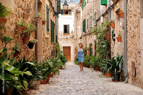 Beautiful pretty woman walking at old town pavement street with flowers and looking away. Travel concept