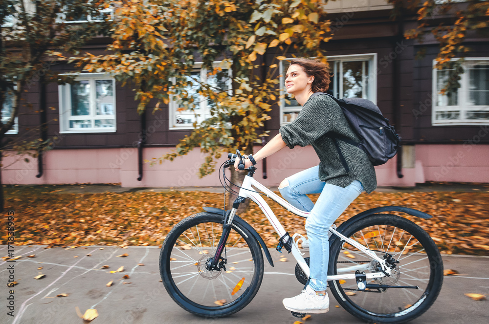 Beautiful young female student in a sweater and jeans on a bicycle on the street