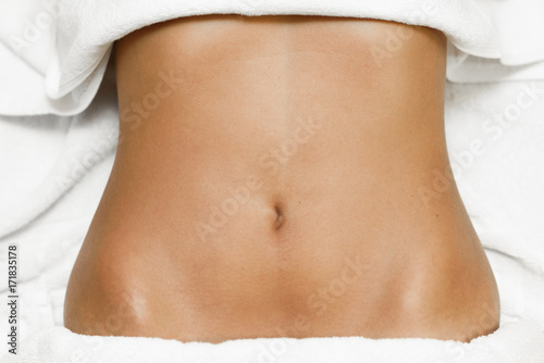 Top view of female abdomen laying on spa bed with white towels.