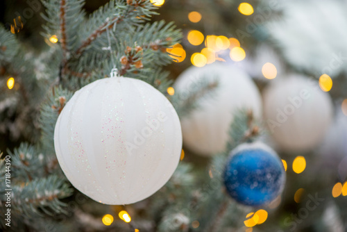 Close-up detail of a white, glittery Christmas oranment on a pale spruce tree, with bokeh lights in the background, Singapore. Xmas and family celebration concept. photo