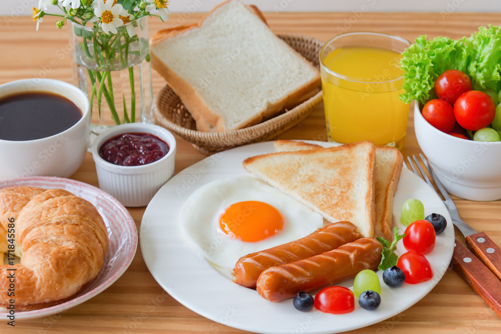 Homemade breakfast with sunny side up fried egg toast sausage fruits vegetable strawberry jam and orange juice in top view with copy space.Delicious homemade american breakfast concept for background