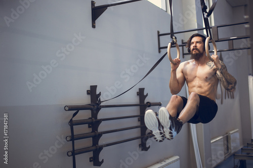 Fitness handsome man doing dipping exercise using rings in the gym photo