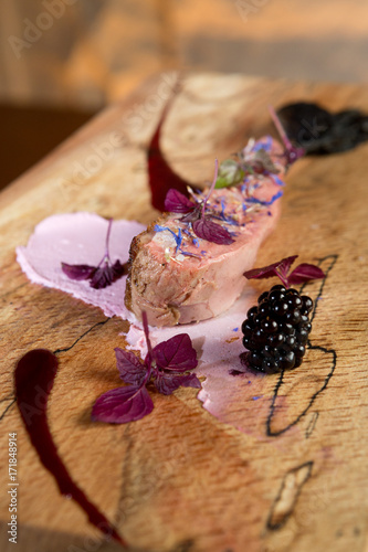 A beautiful succulent organic duck breast slice, served with blackberry puree, thyme and olive oil, on a rustic wooden chopping board. photo