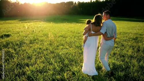 Happy family. Dad mom and a little girl, walking in a field dressed in white under the rays of the setting sun photo