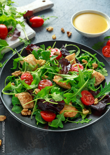 Fresh salad with chicken breast  arugula  nuts and tomatoes on black plate in a wooden table.