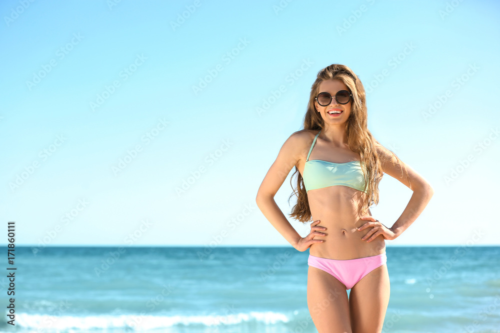 Beautiful young woman in bikini near sea on sunny day