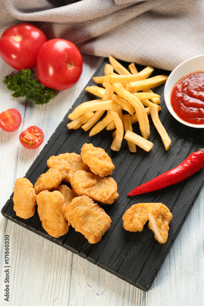 Tasty nuggets, french fries and small bowl with sauce for chicken on wooden board Tasty nuggets, french fries and small bowl with sauce for chicken on wooden board