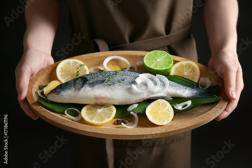 Woman holding wooden dish with fresh fish in hands