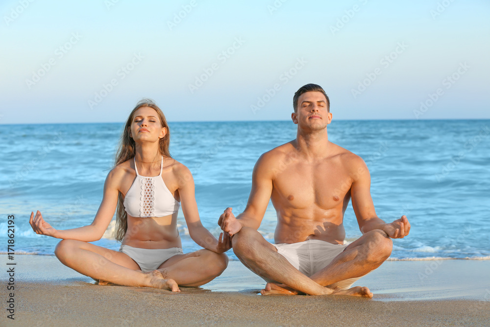 Young couple practicing yoga on sea beach Young couple practicing yoga on sea beach