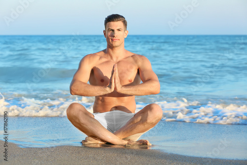 Young man practicing yoga on sea beach