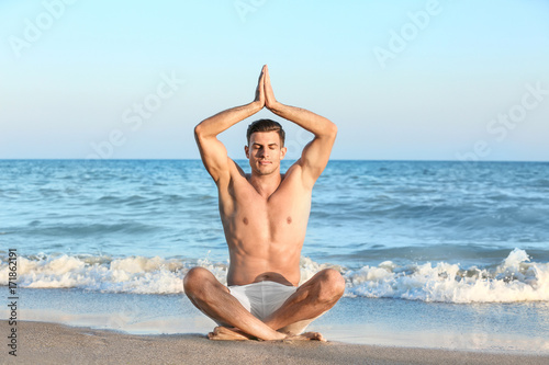 Young man practicing yoga on sea beach