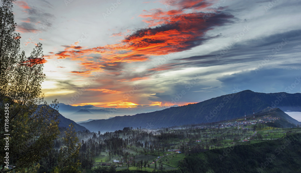 Fototapeta premium Mist flowing over Cemoro Lawang village in the morning located to northeast of Mt Bromo, Indonesia