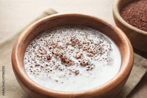 Bowl with boiled quinoa grains and milk on wooden table