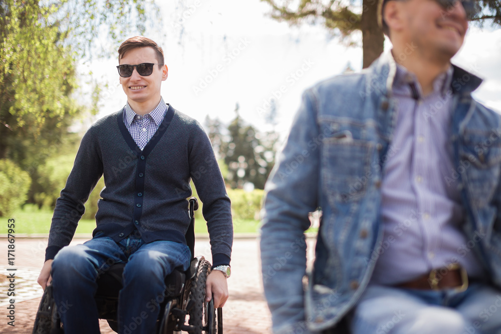 young man sitting on a wheelchair with his friend young man sitting on a wheelchair with his friend