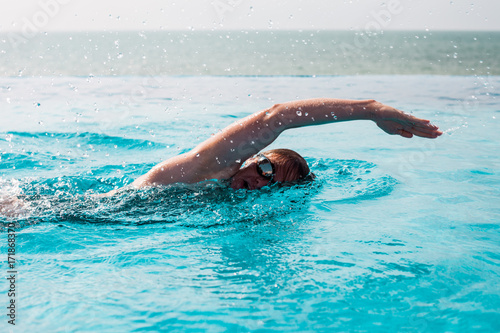 Woman swimming crawl in a pool with sea view