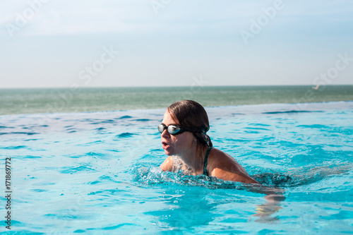 Woman in a swim glasses breaststrokes in a pool with sea view