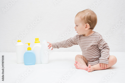 beautiful baby holding a bottle in the hand with shower gel, beside lies Baby cosmetic tubes on white isolated background