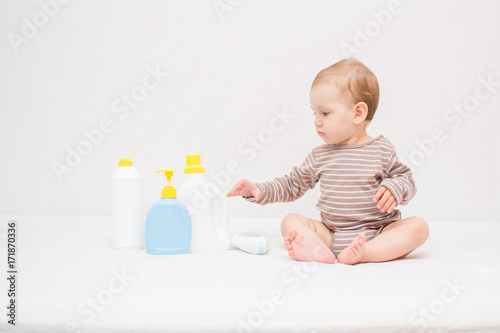beautiful baby holding a bottle in the hand with shower gel, beside lies Baby cosmetic tubes on white isolated background