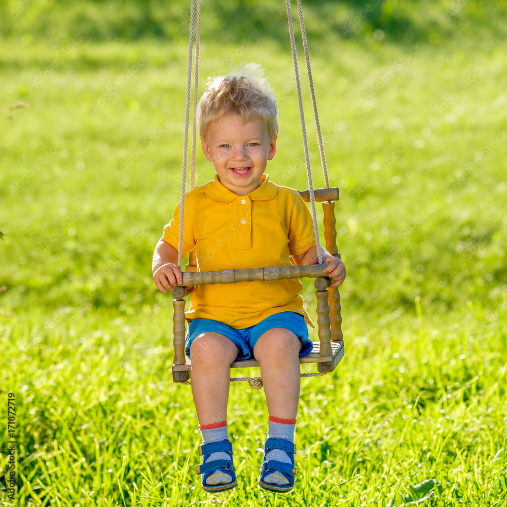Rural scene with toddler boy swinging outdoors.