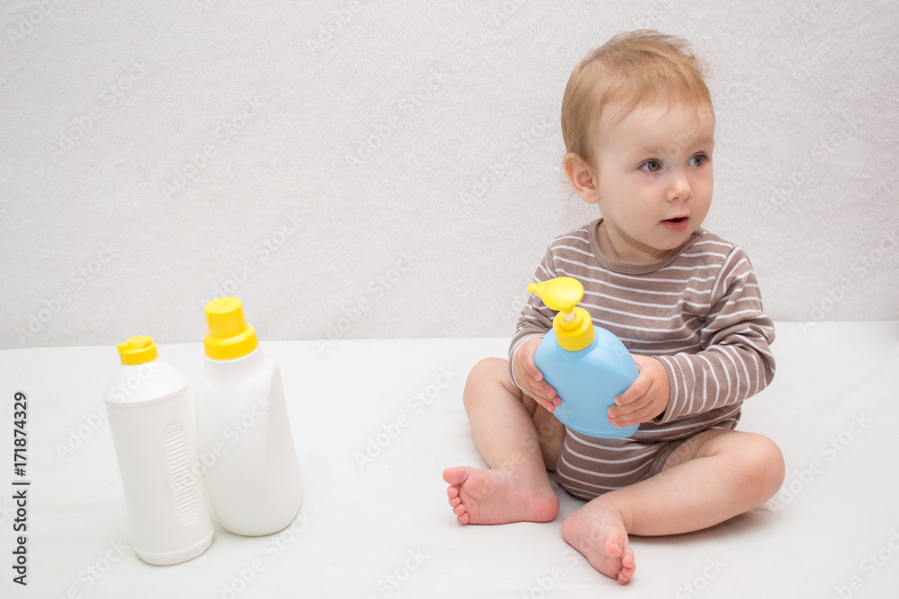 beautiful baby holding a bottle in the hand with shower gel, beside lies Baby cosmetic tubes on white isolated background beautiful baby holding a bottle in the hand with shower gel, beside lies Baby cosmetic tubes on white isolated background
