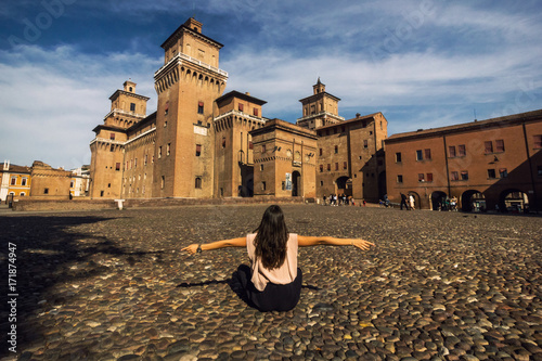 Girl sitting on a cobble-stone street to view Castello Estense of Renaissance town of Ferrara