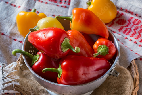 Sweet red peppers in colander on wooden background