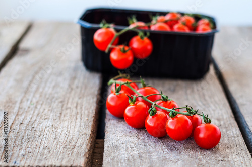 A branch of red organic cherry tomatoes on a wooden background