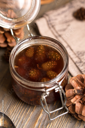 A jar of homemade jam made of pine cones on a dark wooden background.
