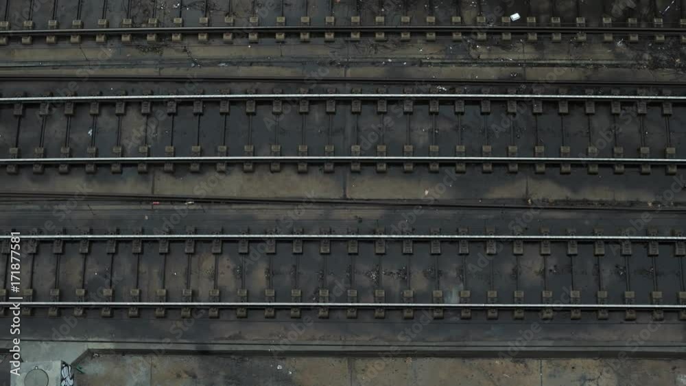 Top view on open railroad or subway tracks in urban industrial district and metro train passing from left to right at rainy weather. Commute concept