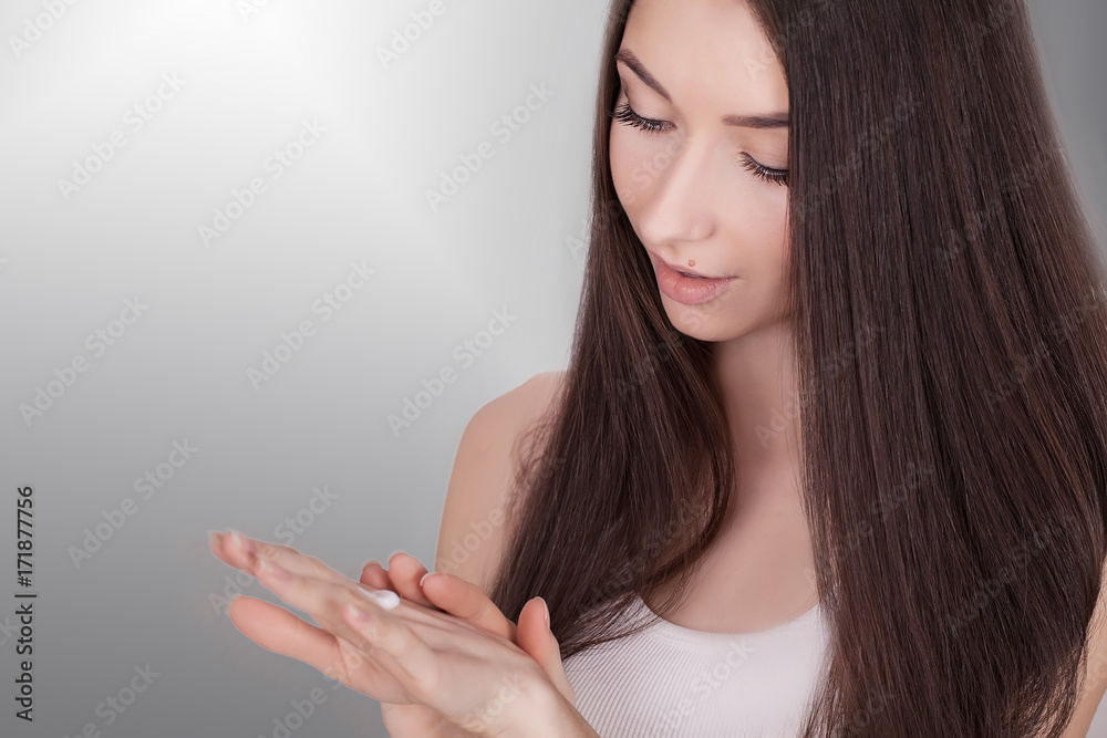 Beautiful young woman applying face cream to her cheek bone in a beauty skincare or cosmetics concept on grey with copy space Beautiful young woman applying face cream to her cheek bone in a beauty skincare or cosmetics concept on grey with copy space