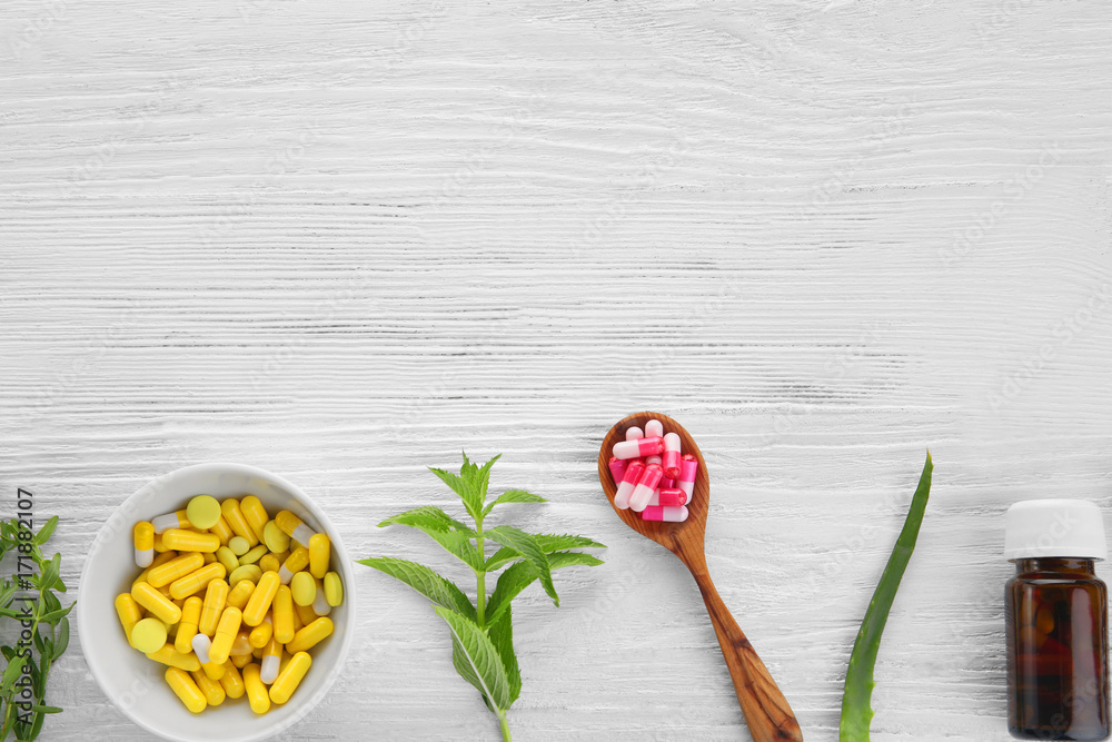 Colorful pills and herbs on wooden background